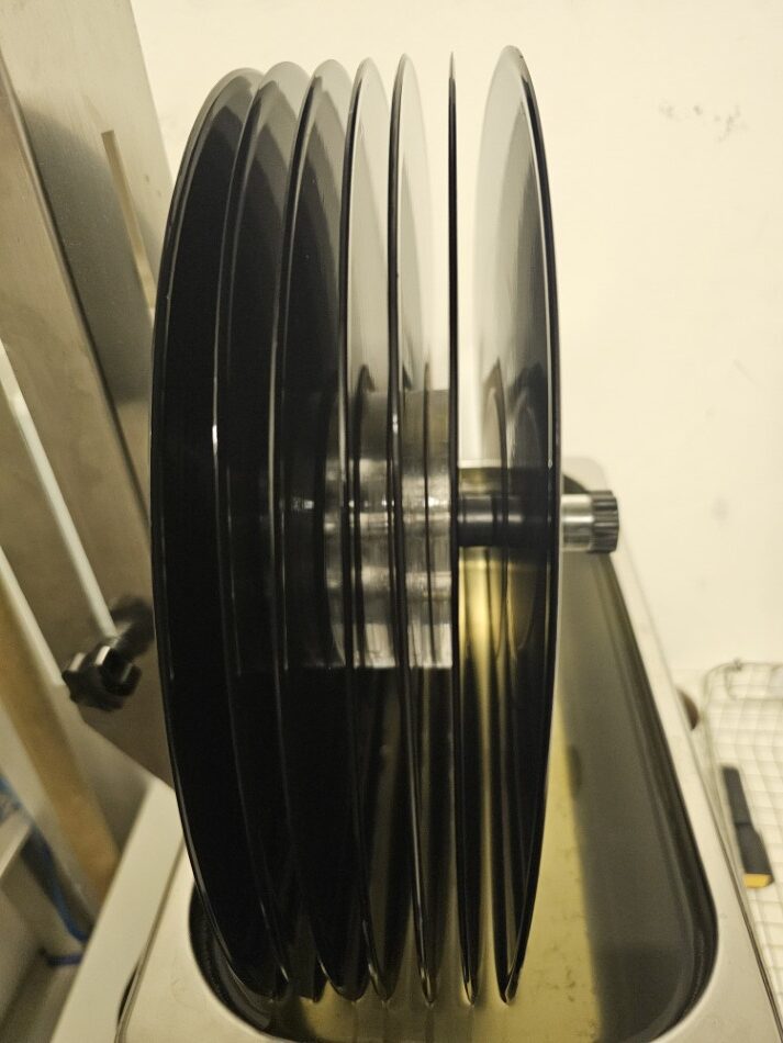 Discos de vinil empilhados em um suporte para limpeza ultrassônica, com líquido de limpeza visível abaixo.